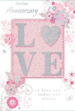 This anniversary card offers a gentle celebration of enduring romance, crafted in the kind of soft palette that would feel at home in a Biggin Hill sitting room filled with fresh flowers. The main feature is the word LOVE, elegantly spelled out in raised, soft glitter that adds a noticeable but refined sparkle, while the letter O is transformed into a shimmering heart, richly textured in silver. The heart catches the light in a slightly different way to the surrounding letters, giving the impression of a cherished focal point at the centre of the design. The background is washed in pastel pinks and silvery greys, creating a sense of treasured intimacy and calm. Around the glittering word and heart, delicate blossoms in blush, mauve, and gentle white unfurl with an almost watercolour softness, as though painted by hand. Their fine, flowing outlines suggest the careful touch of a florist composing a romantic bouquet, each petal layered thoughtfully over the next. Small decorative touches-curving swirls, scattered petals, and subtle butterflies-introduce a feeling of movement and whimsy, reminiscent of an English spring garden you might wander near the edges of Biggin Hill on a mild afternoon. The phrases On Our Anniversary and I love you today and always appear in an understated, graceful script that blends harmoniously with the floral artwork. The card's overall composition feels poised and heartfelt, like a quiet toast shared between two people who know each other deeply. It is the kind of keepsake that might be tucked away in a drawer, revisited years later as a reminder of a soft-spoken yet deeply meaningful celebration of love.